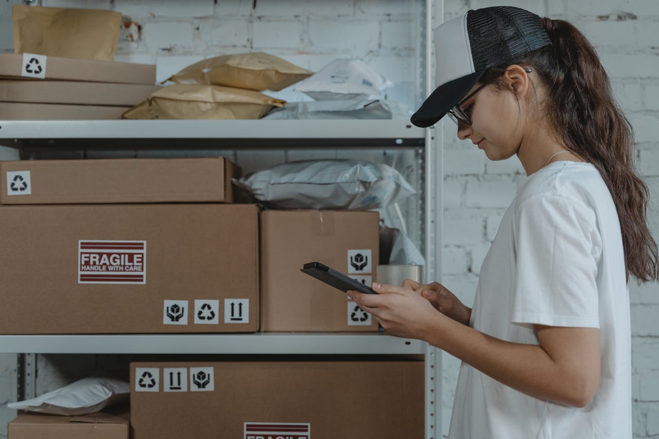 A female courier in uniform managing packages with a device in a storage room.